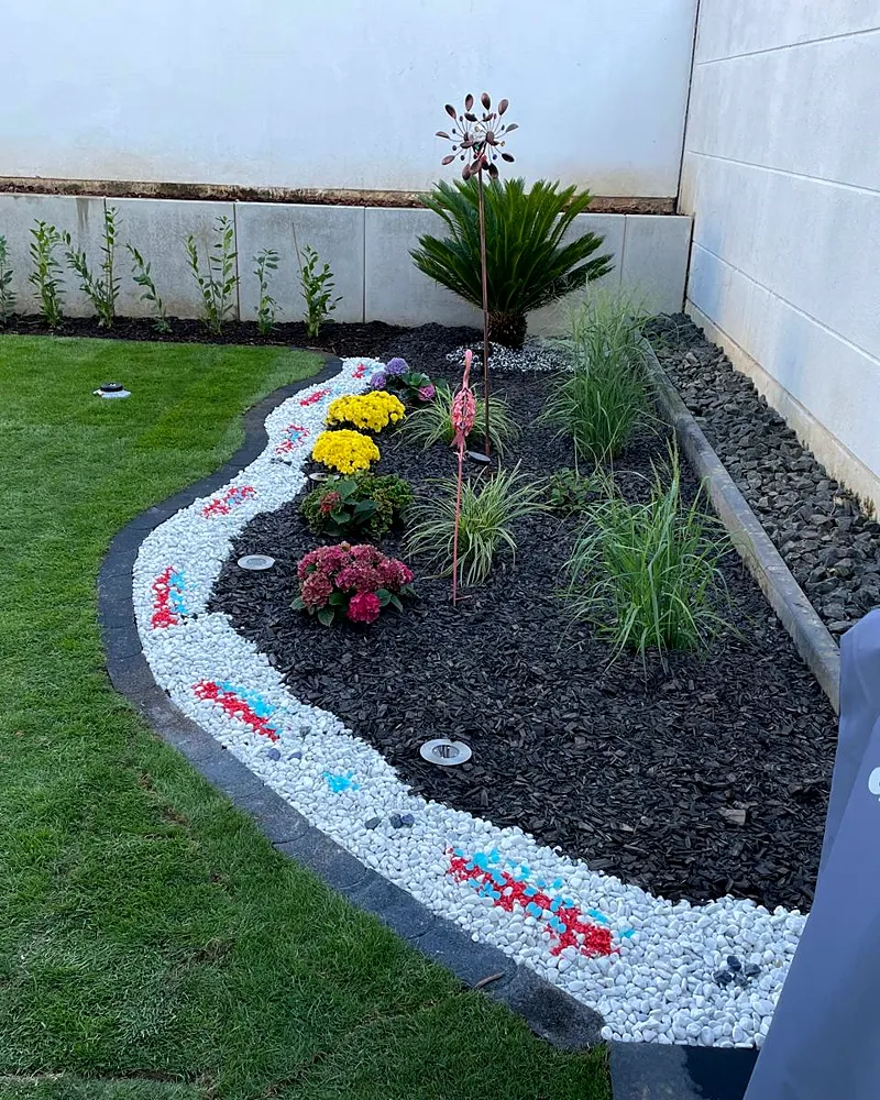 Neu angelegtes Beet mit weißem Zierkies, Rindenmulch und Blumen am Rollrasen