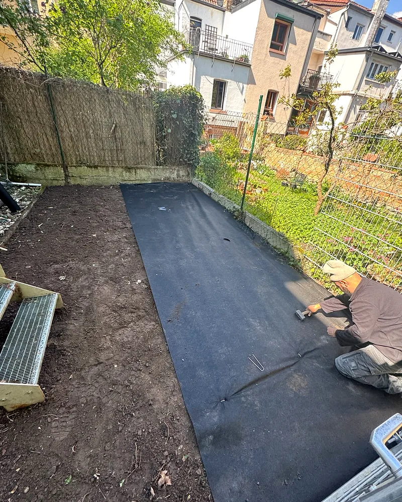 Gartenpflege in Worms: Mitarbeiter von Gezer Bau & Garten verlegt schwarzes Unkrautvlies auf der vorbereiteten Beetfläche