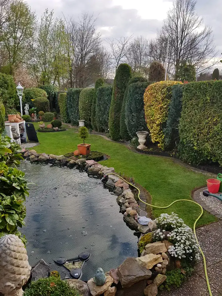 Gartenteich mit Natursteinumrandung und gepflegter Hecke