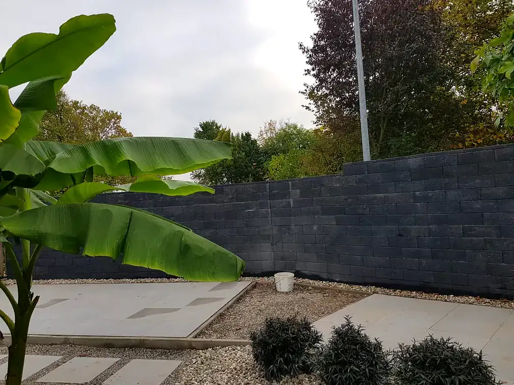 Anthrazitfarbene Natursteinmauer mit Kiesfläche und Bepflanzung
