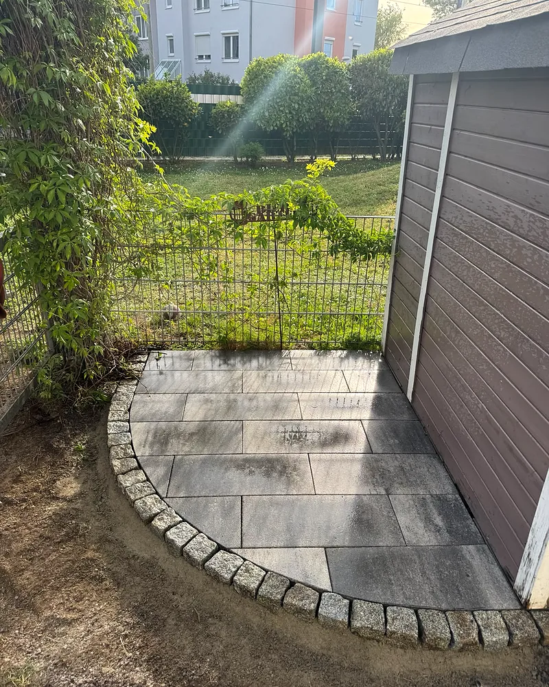 Geschwungene Plattenterrasse aus grauen Betonsteinen mit handgesetzter Granit-Pflastereinfassung hinter dem Gartenhaus, Mannheim