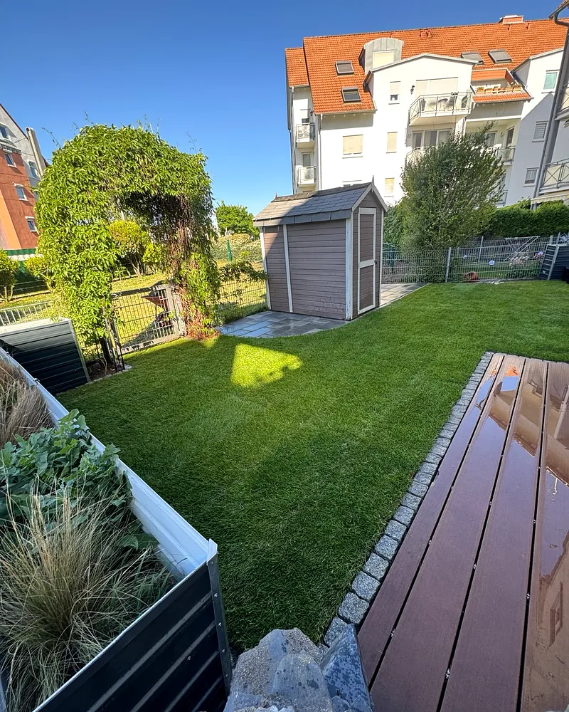 Neu angelegter Rasen mit braunem Gartenhaus und WPC-Terrasse in einer Wohnanlage in Mannheim, im Hintergrund Mehrfamilienhäuser