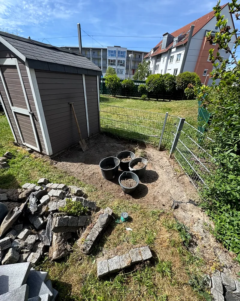 Vorzustand des Gartens in Mannheim: nackter Boden am Gartenhaus, Eimer mit Erde und ein Haufen alter Pflastersteine und Bauschutt