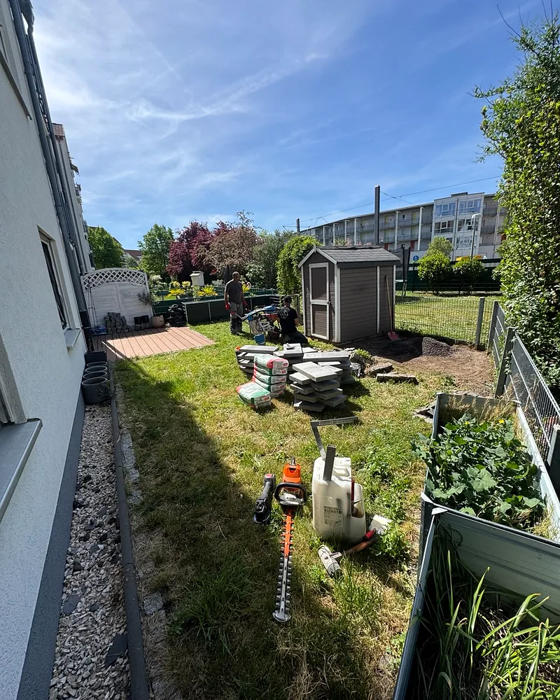 Gartenarbeiten in einer Wohnanlage in Mannheim: zwei Mitarbeiter mit Werkzeug, gestapelte Terrassenplatten und Zementsäcke auf der Wiese