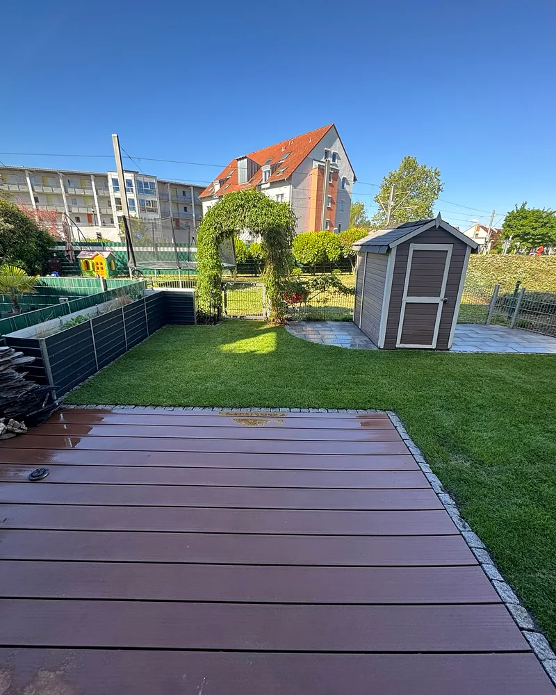 Frisch geölte WPC-Terrassendiele mit Granitstein-Einfassung, dahinter Rasen und Gartenhaus, Wohnanlage in Mannheim